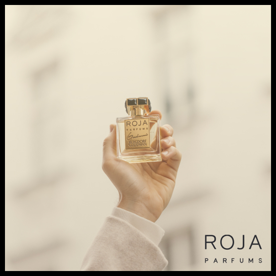 A hand holding a Roja Parfums fragrance bottle against a soft neutral background